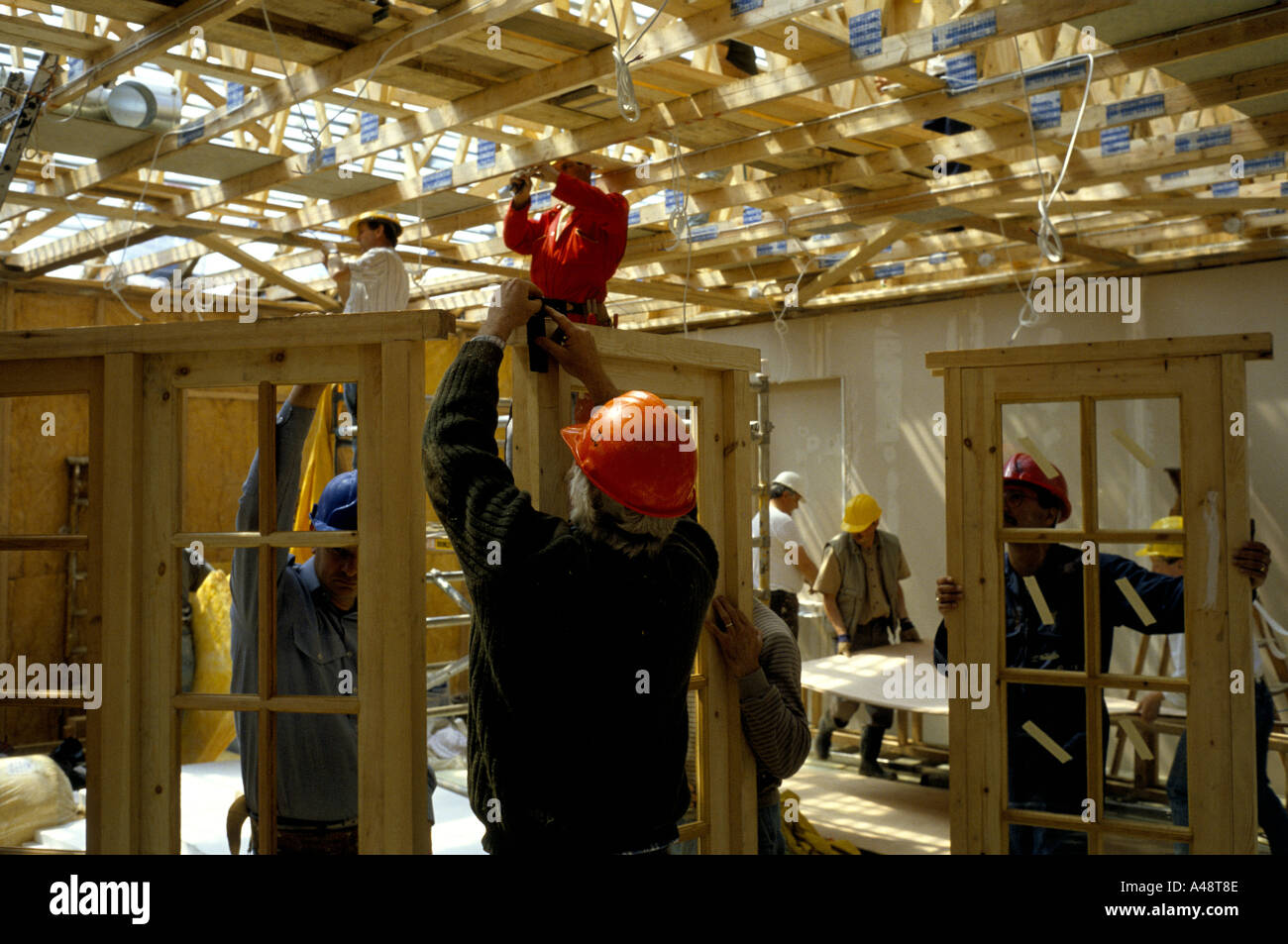Construction workers in hard hats installing window and door frames and ceiling joists in a church hall Stock Photo