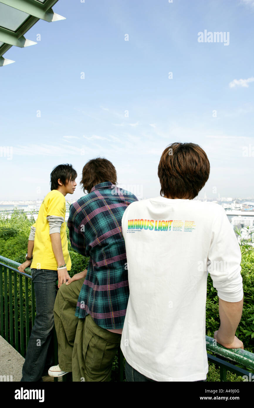 Rear view of three young men standing by a railing Stock Photo - Alamy
