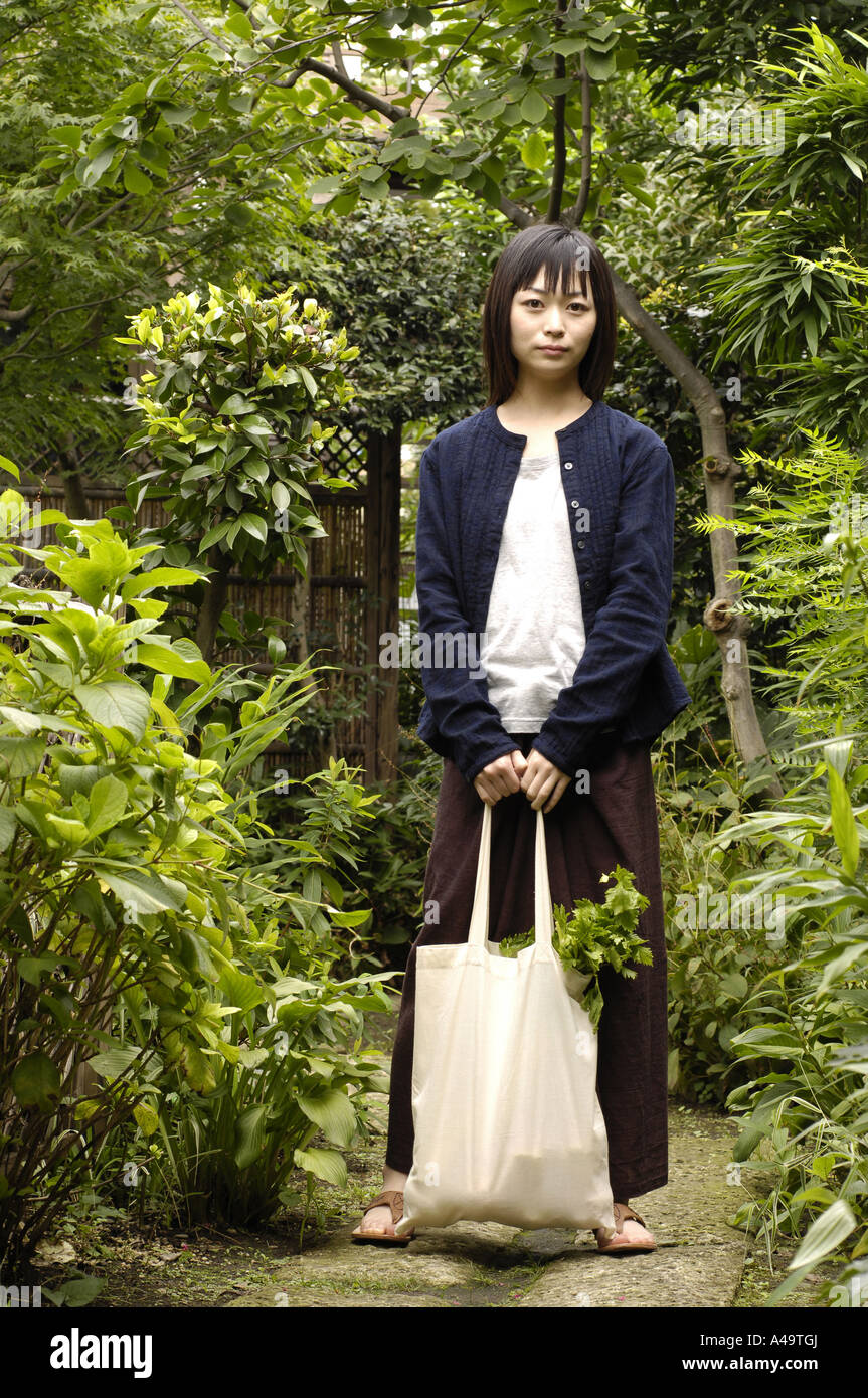 Portrait of a young woman standing in a garden with a bag Stock Photo ...