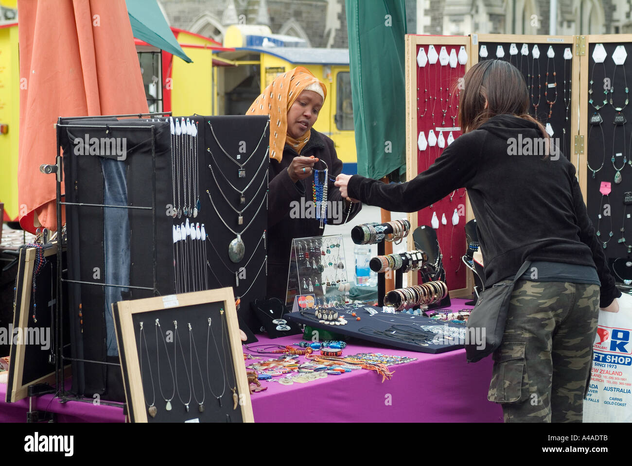 A stall keeper in Christchurch Cathethral square New Zealand sells an item of jewellery The cllient wears a head scarf Stock Photo