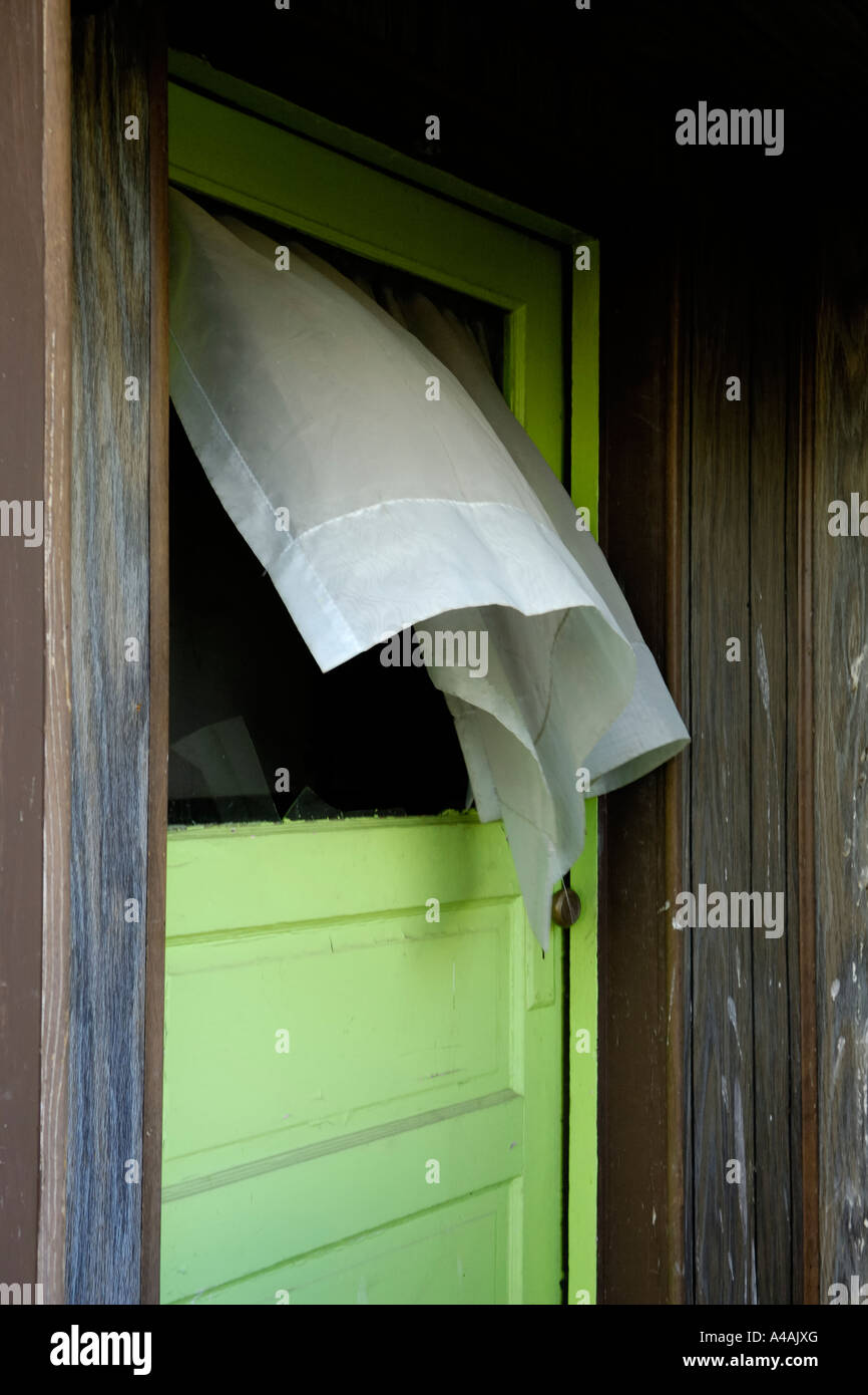 Front door with a broken window and white curtain blowing in the wind