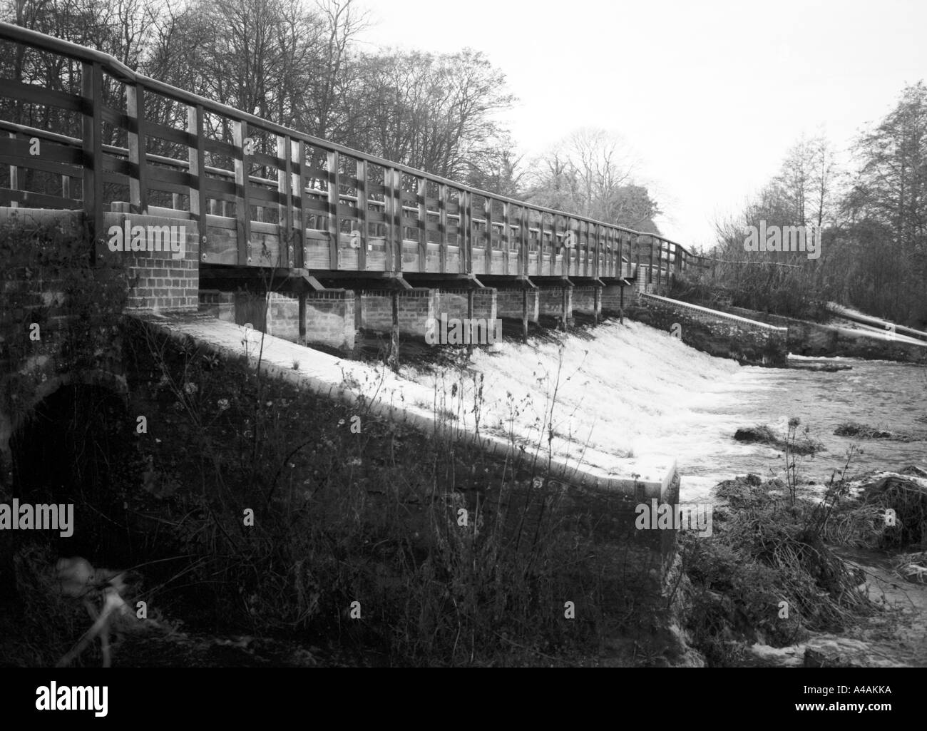 Water rushes over a weir with a wooden walkway on the Kennet and Avon Canal Stock Photo