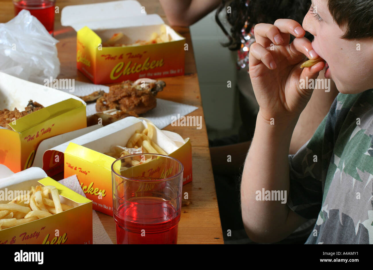 An eight year old boy eating chips covered in tomato ketchup at home