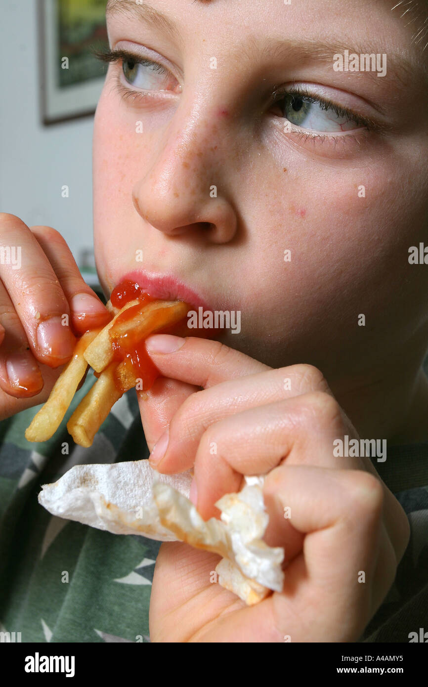 An eight year old boy eating chips covered in tomato ketchup, February