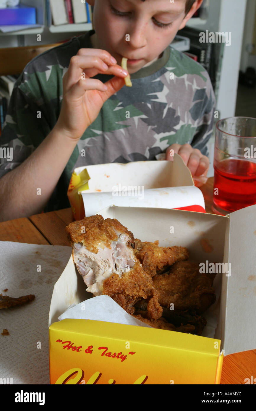 An eight year old boy eating a take away of fried chicken, chips and a