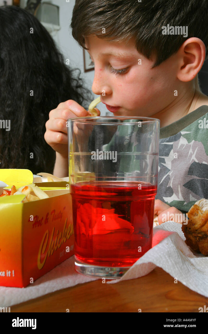 An eight year old boy eating a take away of fried chicken, chips and a