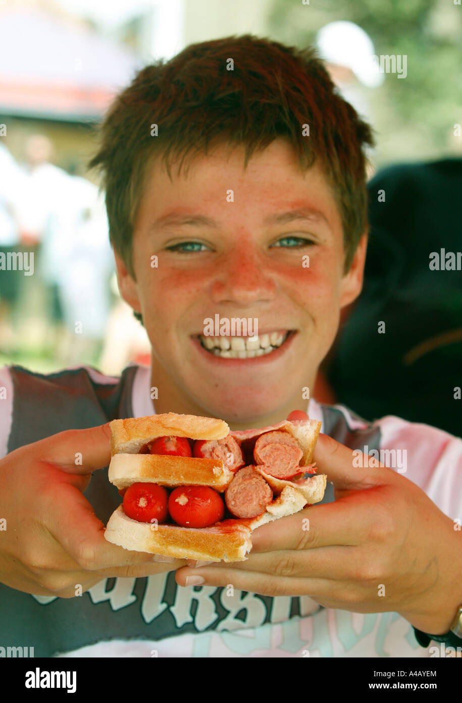 A growing happy teenage boy with a big carbohydrate sandwich with white bread and saveloys or sausages and tomato sauce Stock Photo