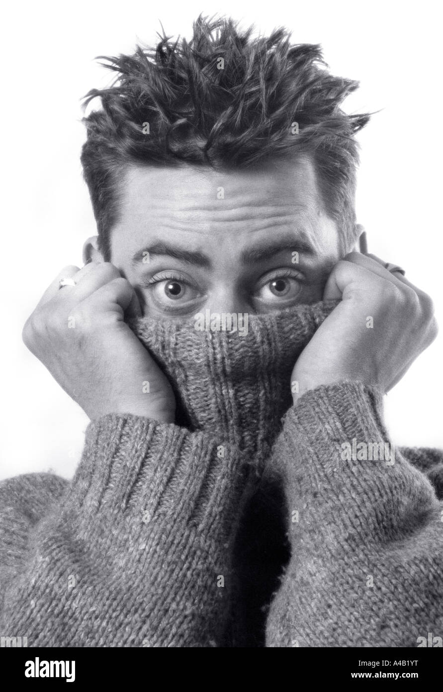 man hiding under jumper pullover james dean photograph famous wide-eyed wide eyes monochrome studio white background nervous shy Stock Photo