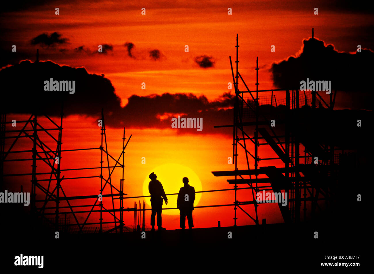 Two workmen silhouetted against setting sun working at height on a building construction site Cardiff Wales UK Stock Photo
