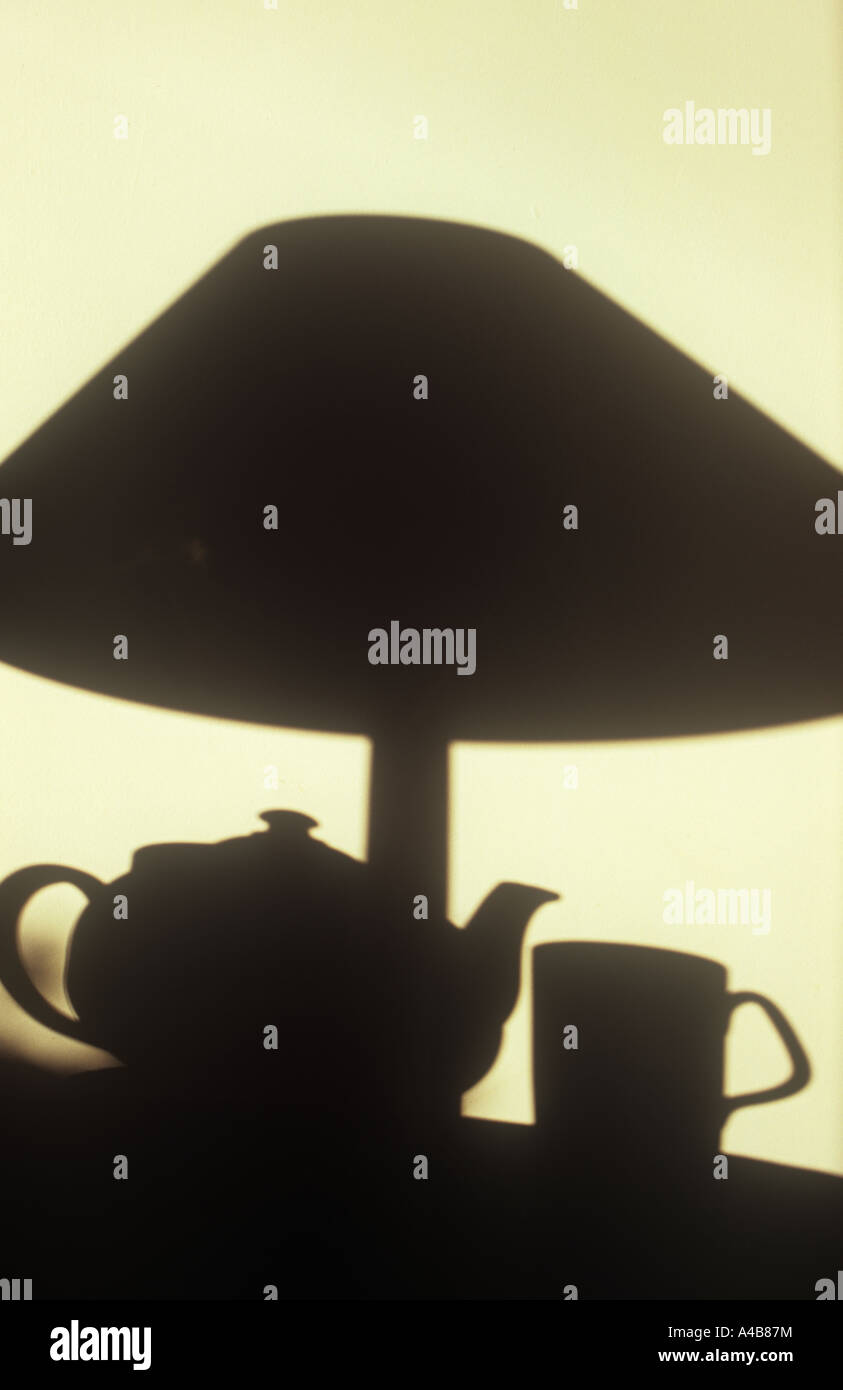 Shadow on cream wall in warm light of teapot with mug and table lamp Stock Photo