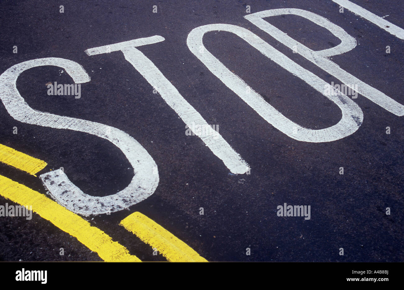 Detail of black tarmac road surface with Stop painted on it and part of a curved double yellow no parking line Stock Photo