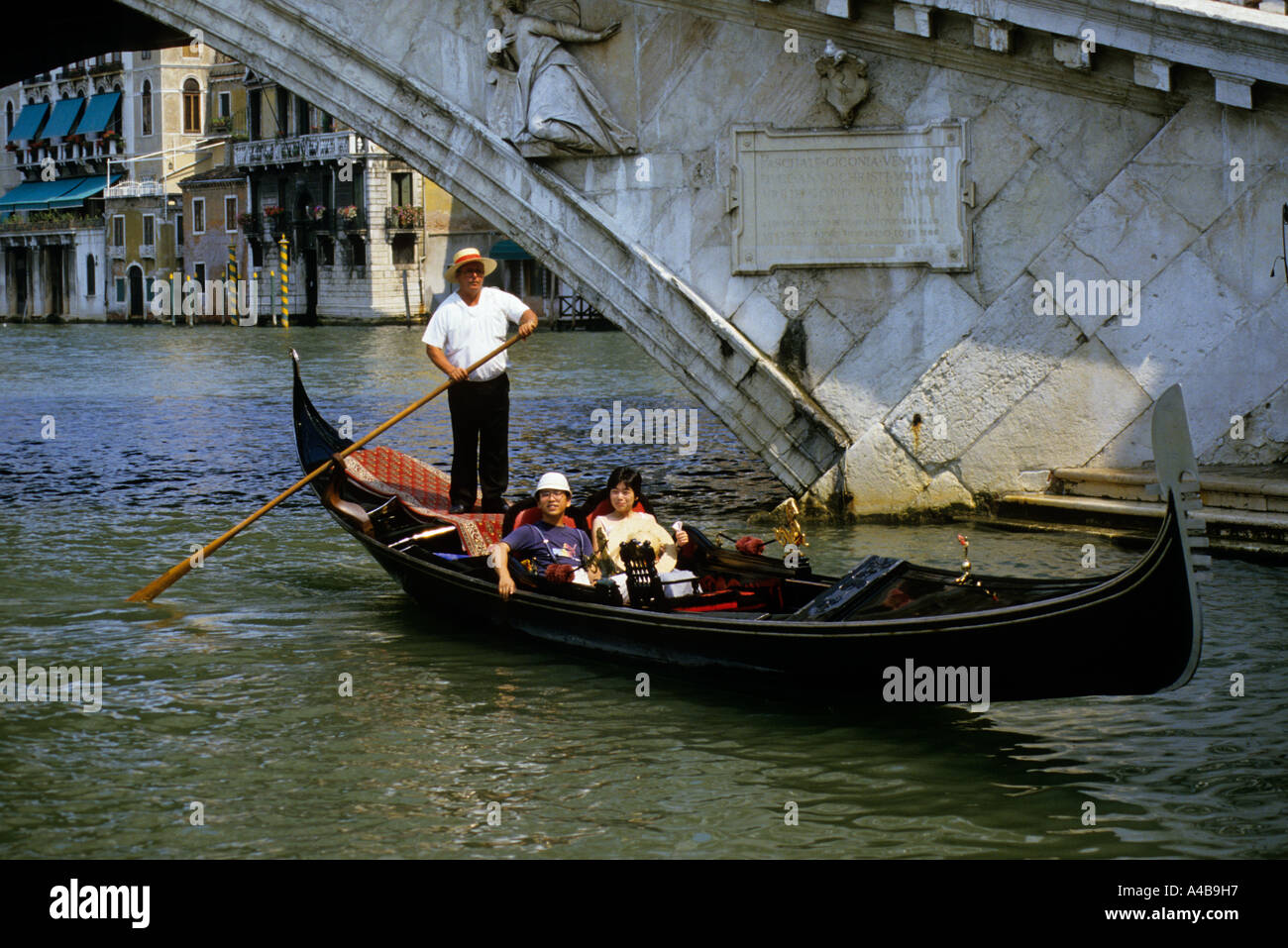 Gondola with Japanese tourists passing beneath bridge Venice Italy Stock Photo