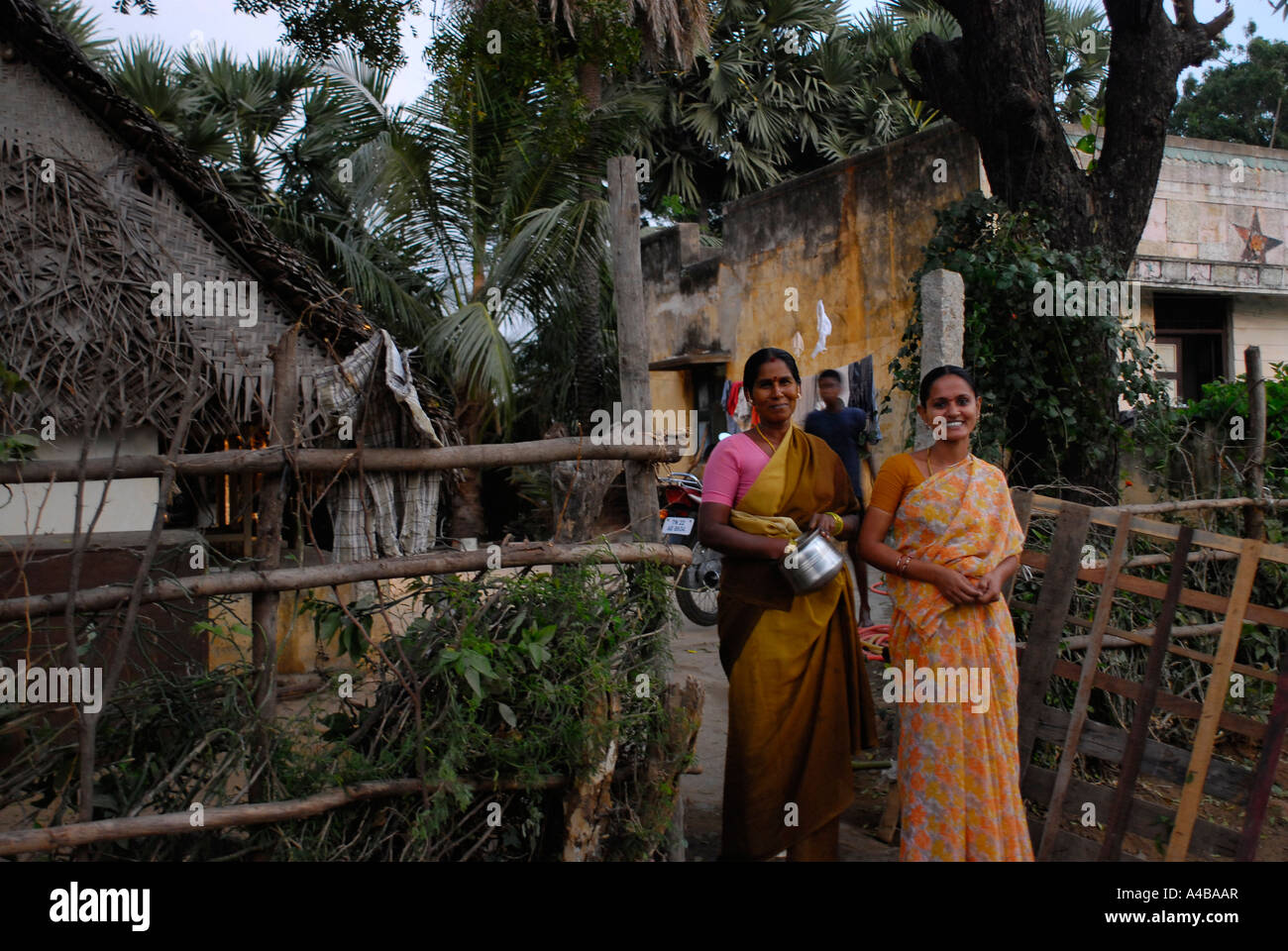 Two Indian tribal Dalit women in saris outside of typical village thatched roof house Stock Photo
