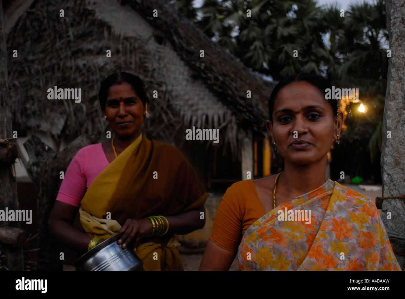 Two Indian tribal Dalit women in saris outside of typical village thatched roof house Stock Photo