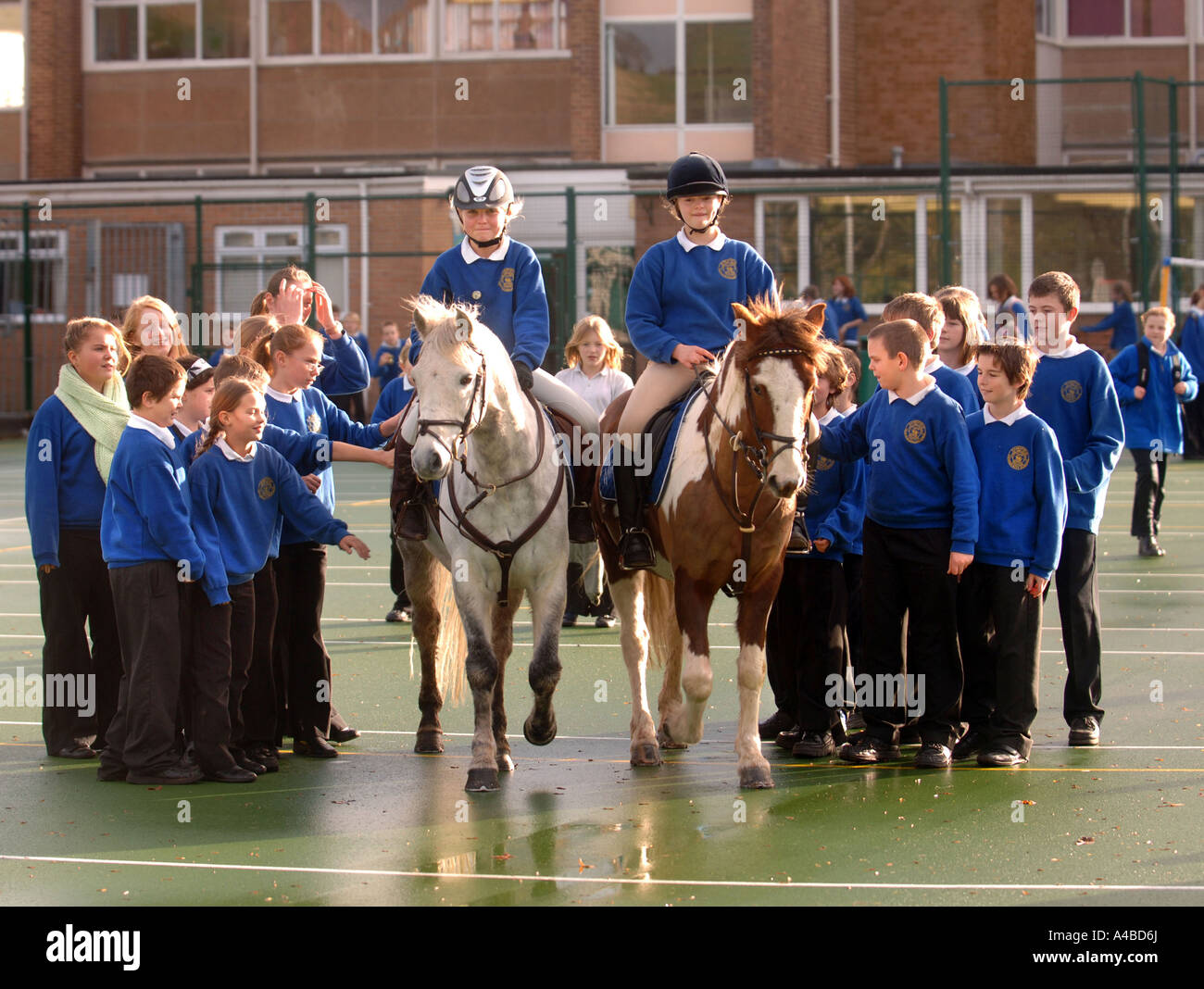 TWO SCHOOL GIRLS ON HORSES IN A PLAYGROUND AT A JUNIOR SCHOOL SOMERSET UK Stock Photo