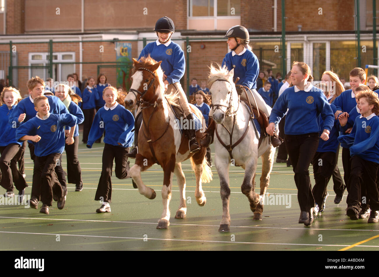TWO SCHOOL GIRLS ON HORSES IN A PLAYGROUND AT A JUNIOR SCHOOL SOMERSET