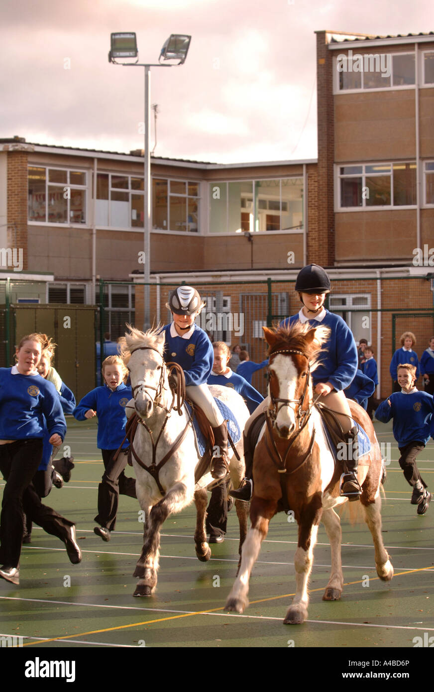 TWO SCHOOL GIRLS ON HORSES IN A PLAYGROUND AT A JUNIOR SCHOOL SOMERSET