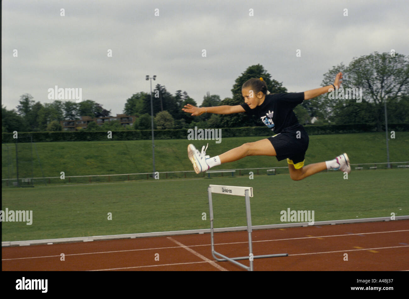 girl jumping hurdle on running track at athletics training session for