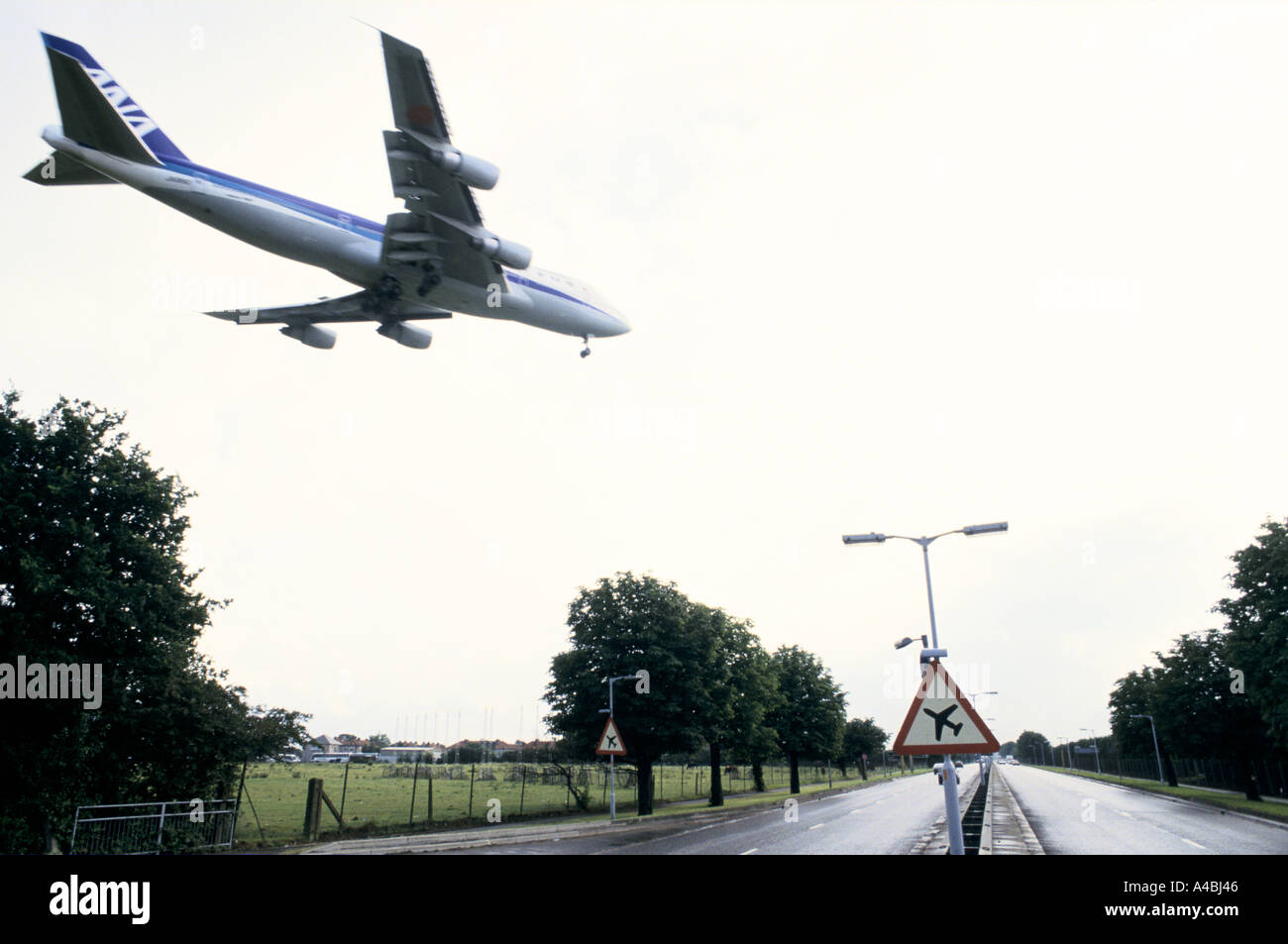 Aircraft coming in to land at London Heathrow airport flies over A4 past a sign warning of low flying aircraft near Hatton Cross Stock Photo