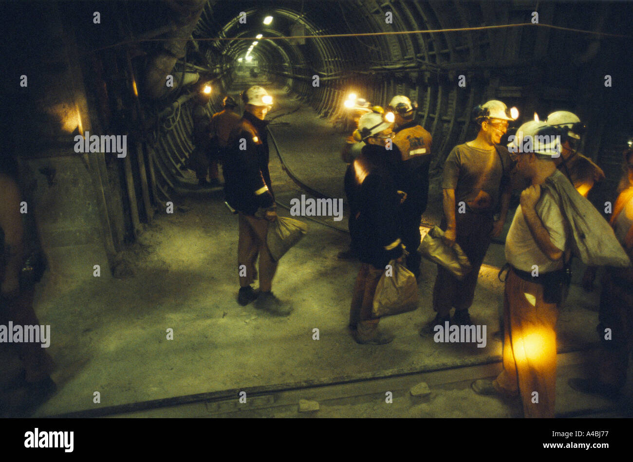 COALMINERS CHATTING WITH HEADTORCHES ON IN UNDERGROUND TUNNEL, CARRYING PAPER BAGS, Stock Photo