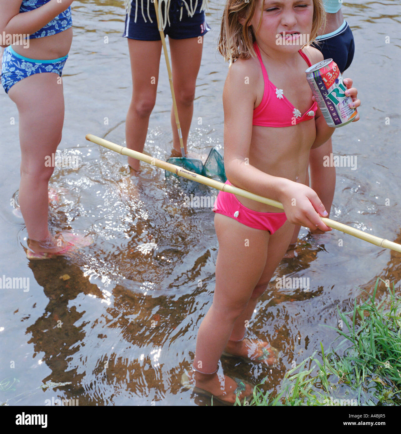 Girl playing with friends drinking a fizzy drink while fishing for tadpoles Stock Photo