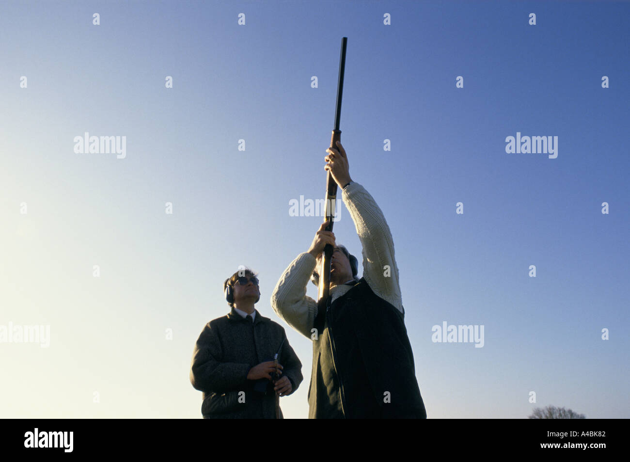CLAY PIGEON SHOOTING, AIMING SHOTGUN INTO CLEAR BLUE SKY, ENGLAND, 1990 Stock Photo