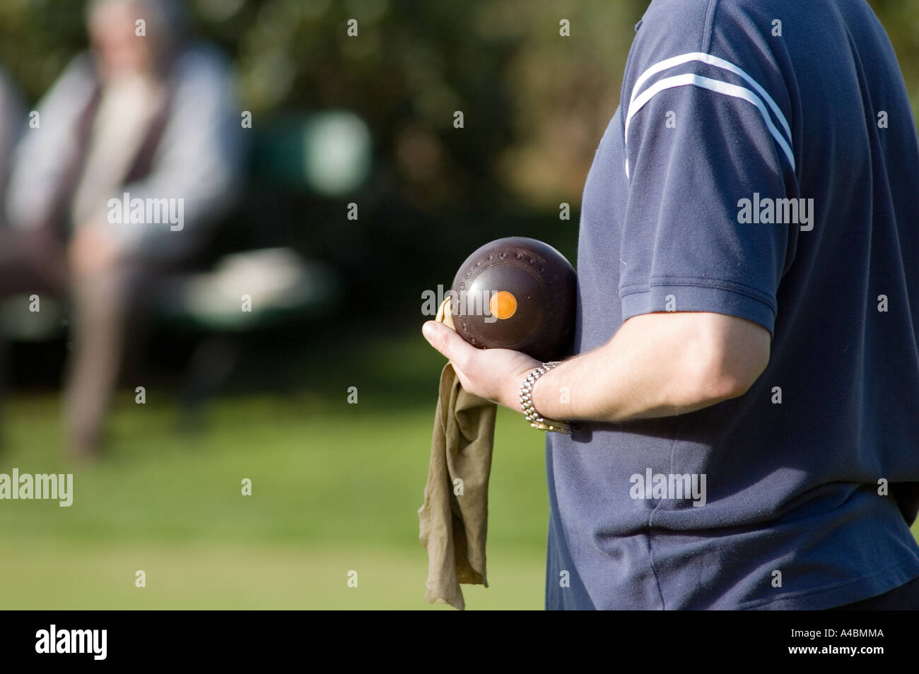A profile of a young male crown green bowler on a sunny day in England with bowl in hand contemplating his shot with spectators Stock Photo