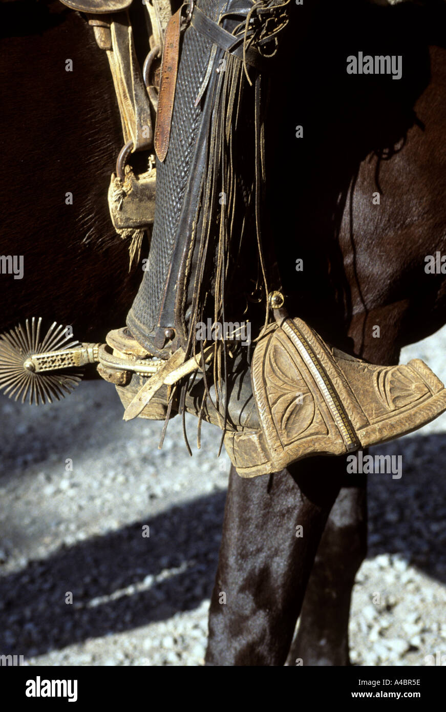 Southern Chile. Traditional old-fashioned carved wooden stirrups, spurs and embossed leather leg guard worn by a gaucho. Stock Photo