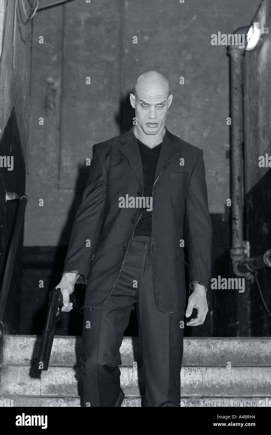 Sinister male figure holding gun walks down steps in urban setting (scene from horror short film Welcome to Hell) Stock Photo