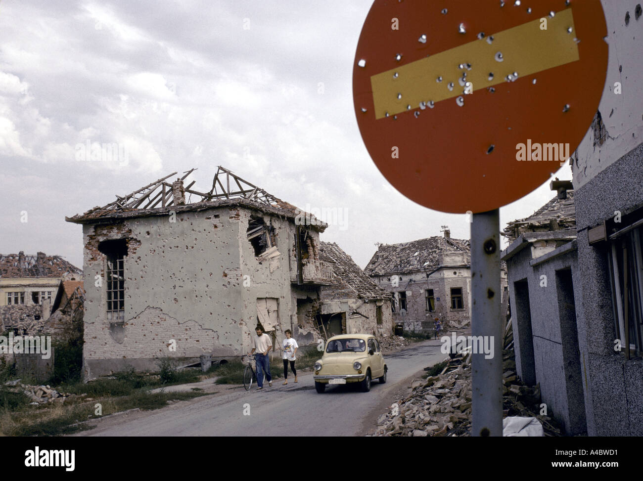 Vukovar, Croatia, under Serb control,  Feb 1992: people walk along a street of burnt out remains of houses pitted with shellfire Stock Photo