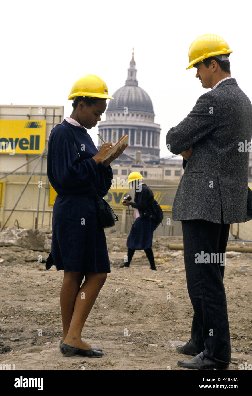 SIXTH FORM SCHOOL GIRLS WITH SAFETY HAT ON VOCATIONAL TRAINING INTERVIEWING SITE MANAGER ON BUILDING SITE. Stock Photo
