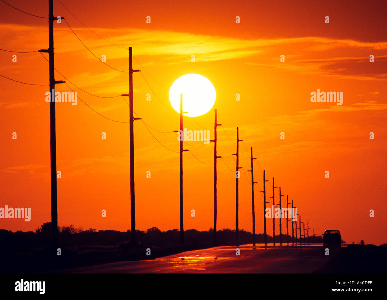 A car drives down a lonely road at sunset Stock Photo