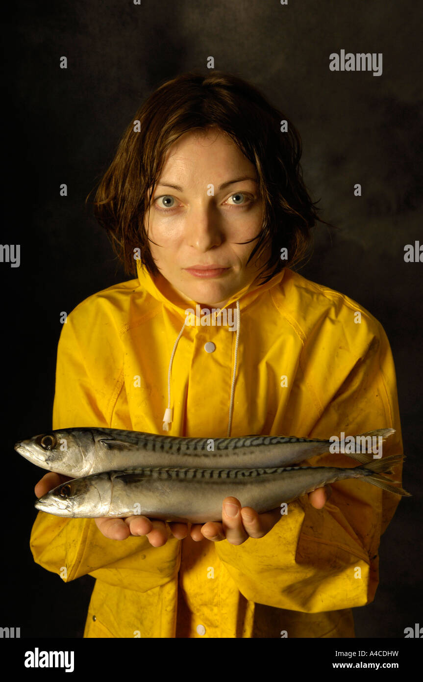 A woman in yellow oilskins holding raw fish Stock Photo