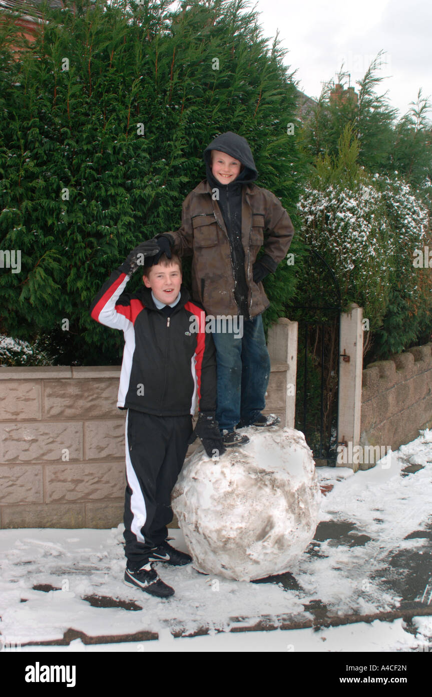 Two Boys With The Giant Snowball That They Have Made Together. Stock Photo