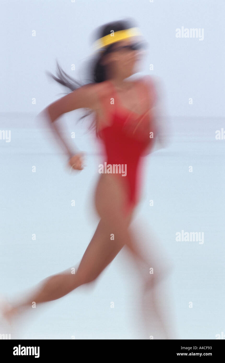 Woman in red swimsuit jogging along beach Stock Photo