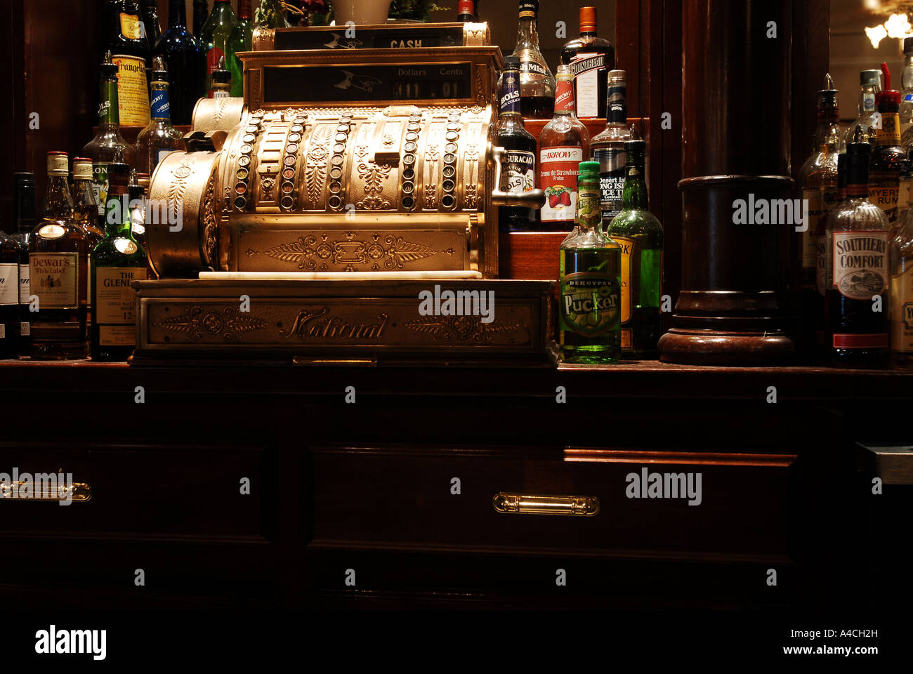 An antique brass mechanical cash register at a bar with bottles of