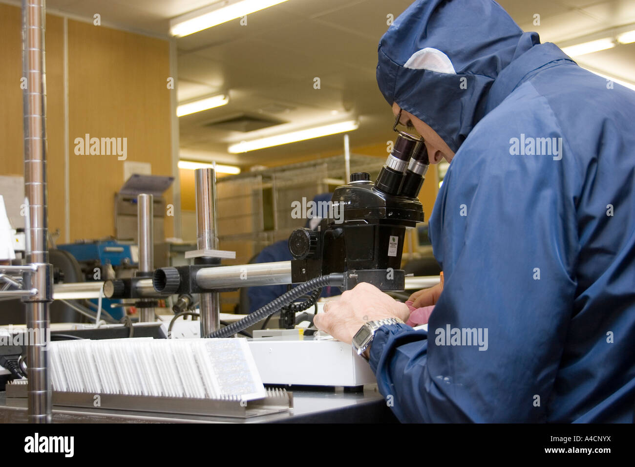 Technician peers through microscope as he works on micro circuit at CMac Micro Electronics in Great Yarmouth, England Stock Photo
