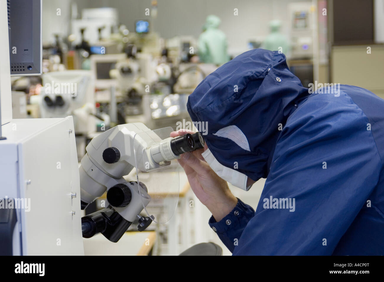 Technician peers through microscope in  clean room lab at CMac Micro Electronics in Great Yarmouth, England Stock Photo