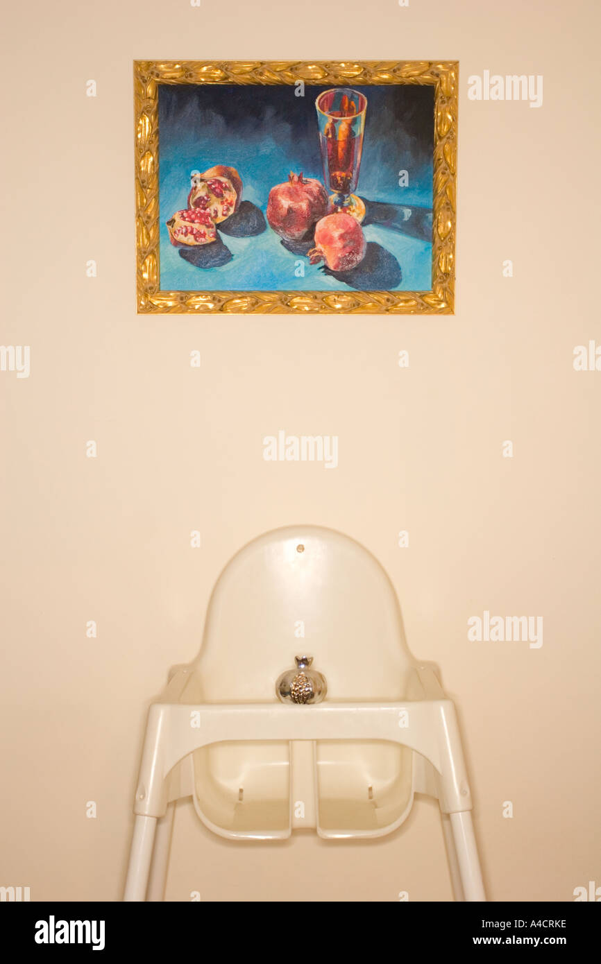 Plastic baby chair with silver metal pomegranate on it, under one painting of pomegranates on the wall above it. Pomegranate is Stock Photo
