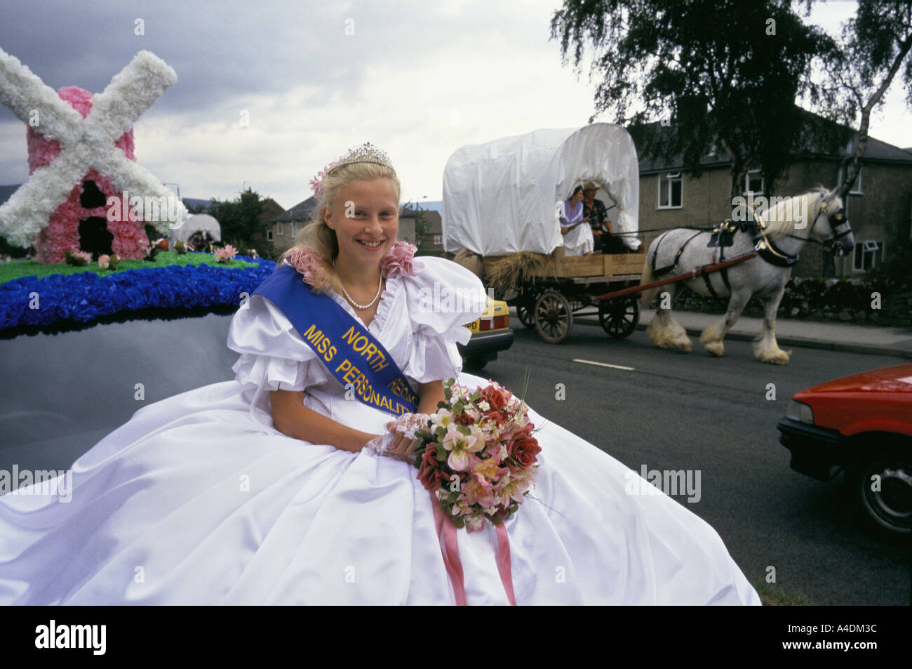 The carnival queen rides by on her float while a coach and horse drives by, Wakes Queen Festival, Bradwell village Stock Photo