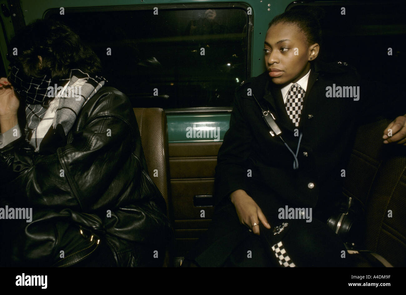 A black policewoman with an arrested woman hiding her face with her scarf on the back of a police van Stock Photo