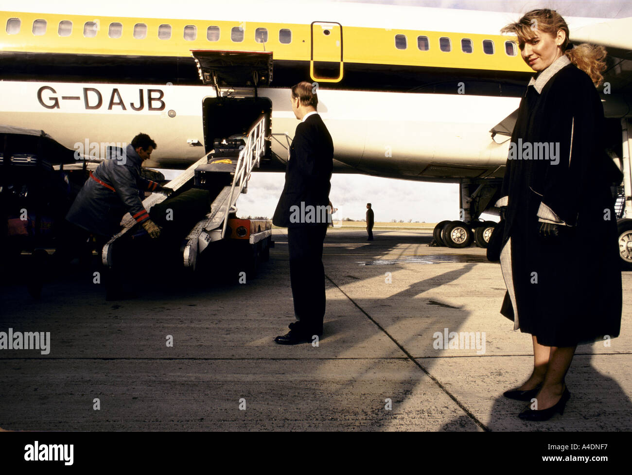 A customs officer watching baggage handlers unloading an aircraft at Stansted airport Stock Photo