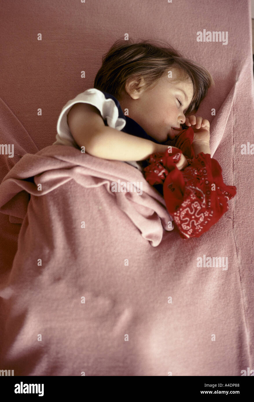 A toddler asleep under a blanket, sucking her thumb while holding a handkerchief. The Creche des Halles in Paris, France Stock Photo