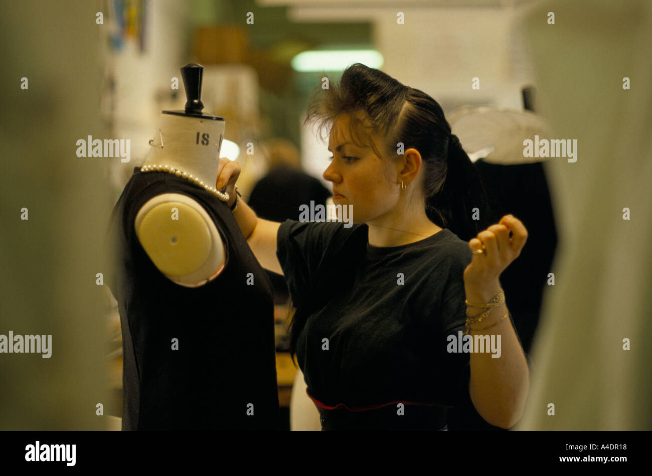 A wardrobe assistant sewing a costume on a mannequin for the