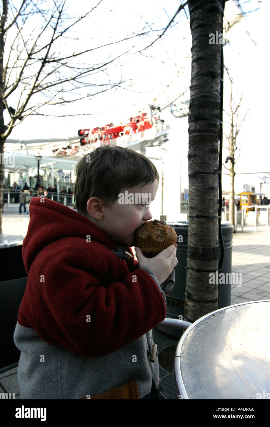 boy aged four tucks into a muffin in the shadow of the London Eye Stock Photo