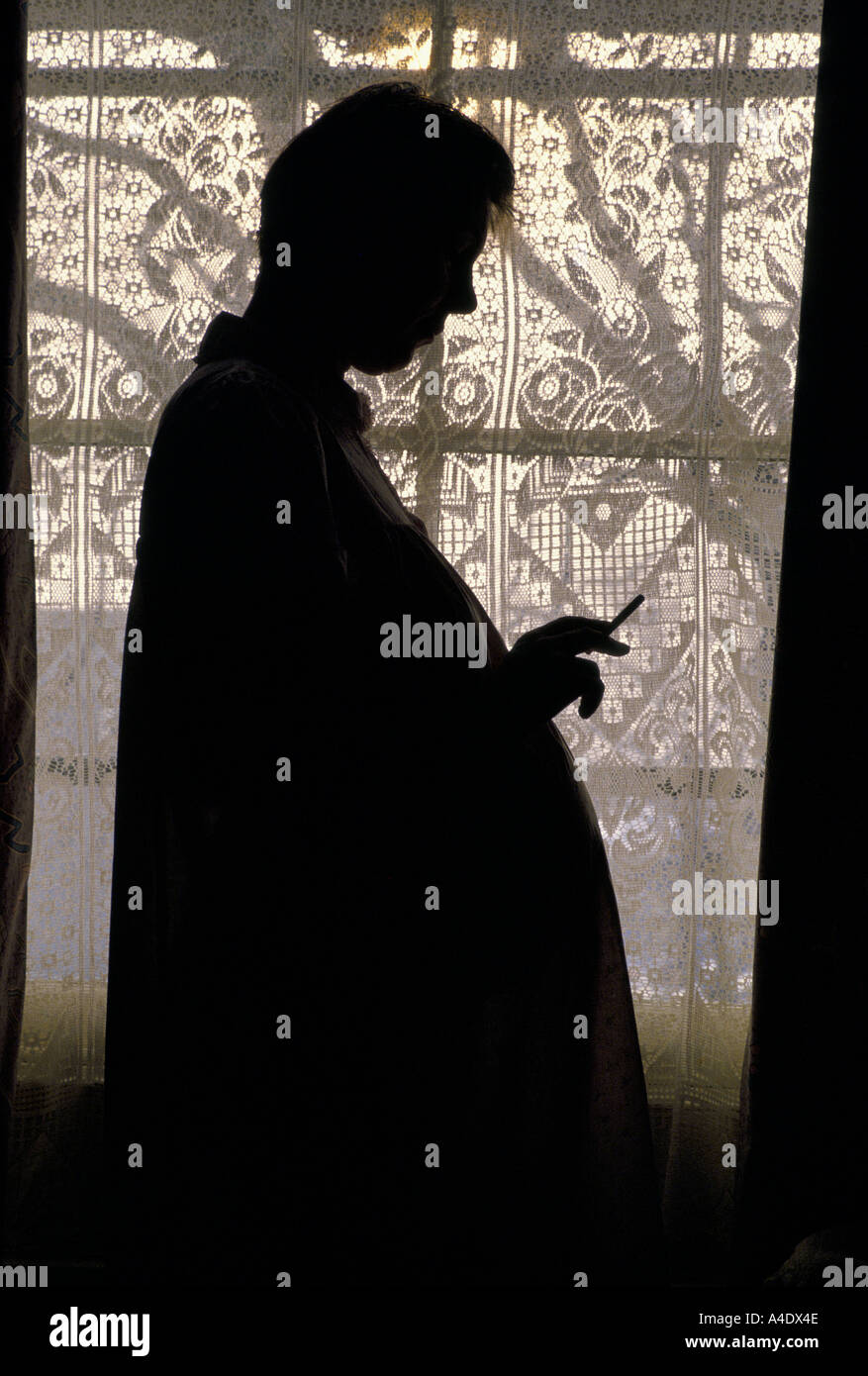 Silhouette of a pregnant woman smoking in front a window in London, UK Stock Photo