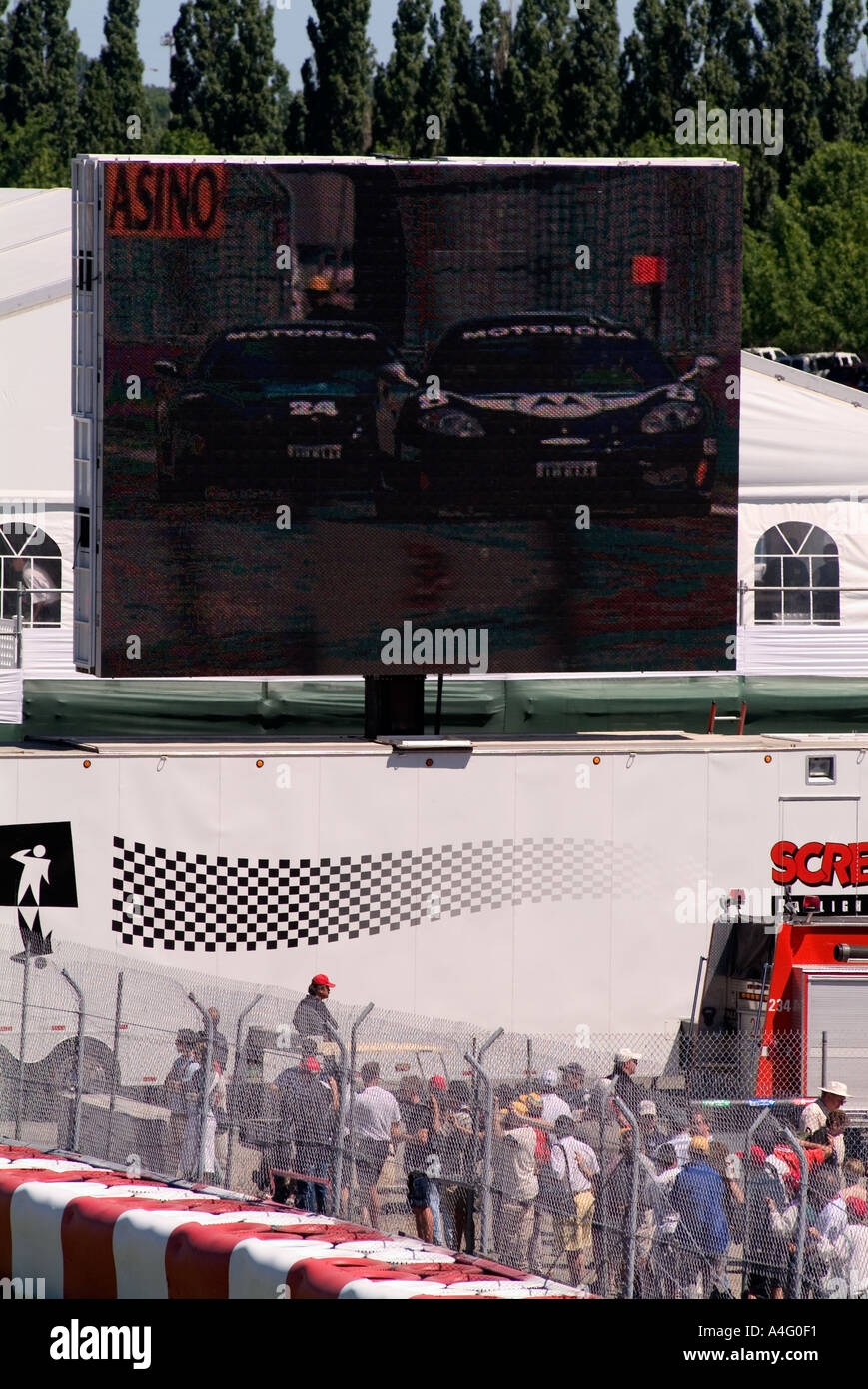 Car race spectator billboard men working below screen Gilles Villeneuve ...