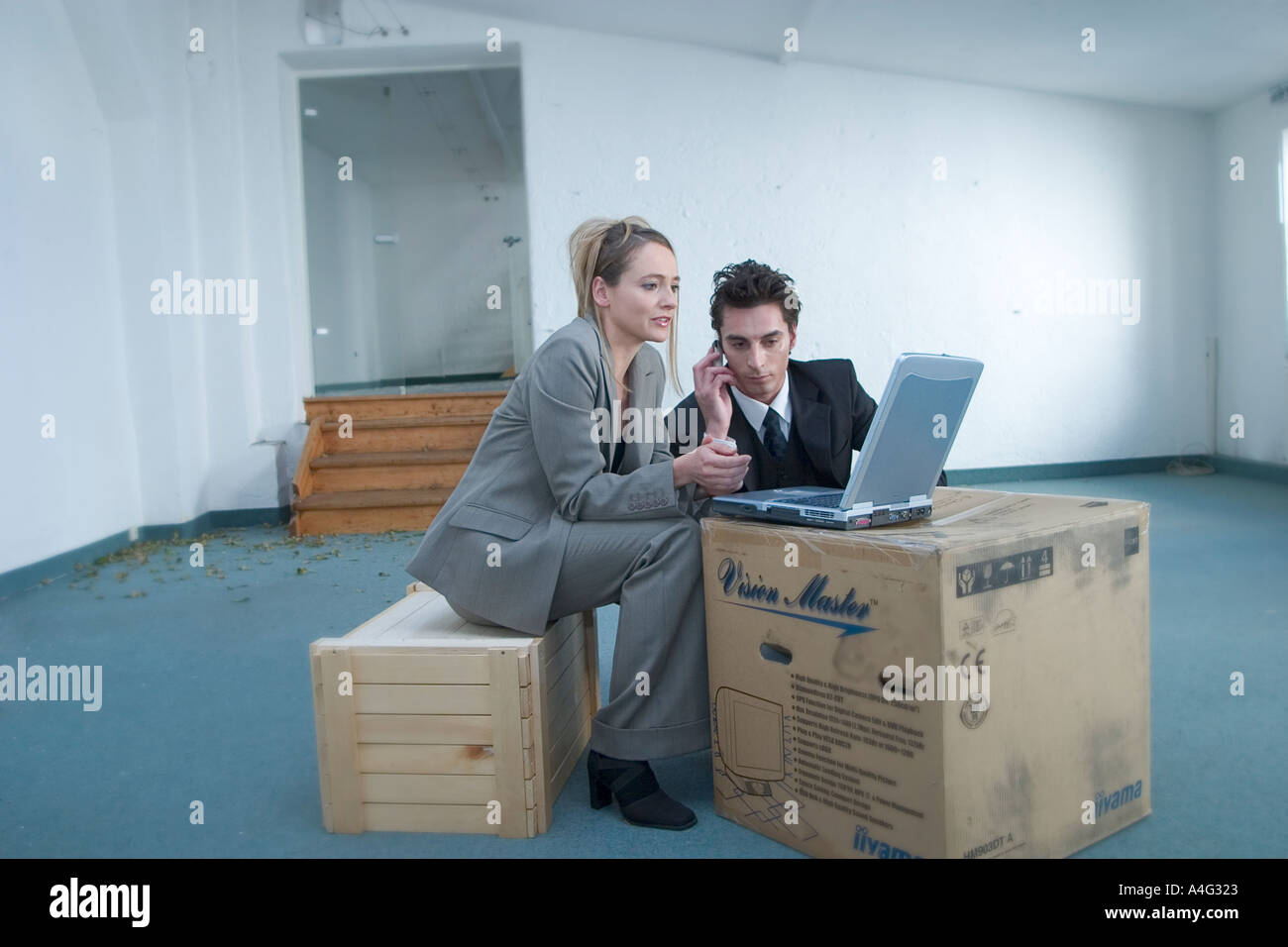 MR Man and woman in business outfit sit in an empty loft at a laptop and talk something over Stock Photo