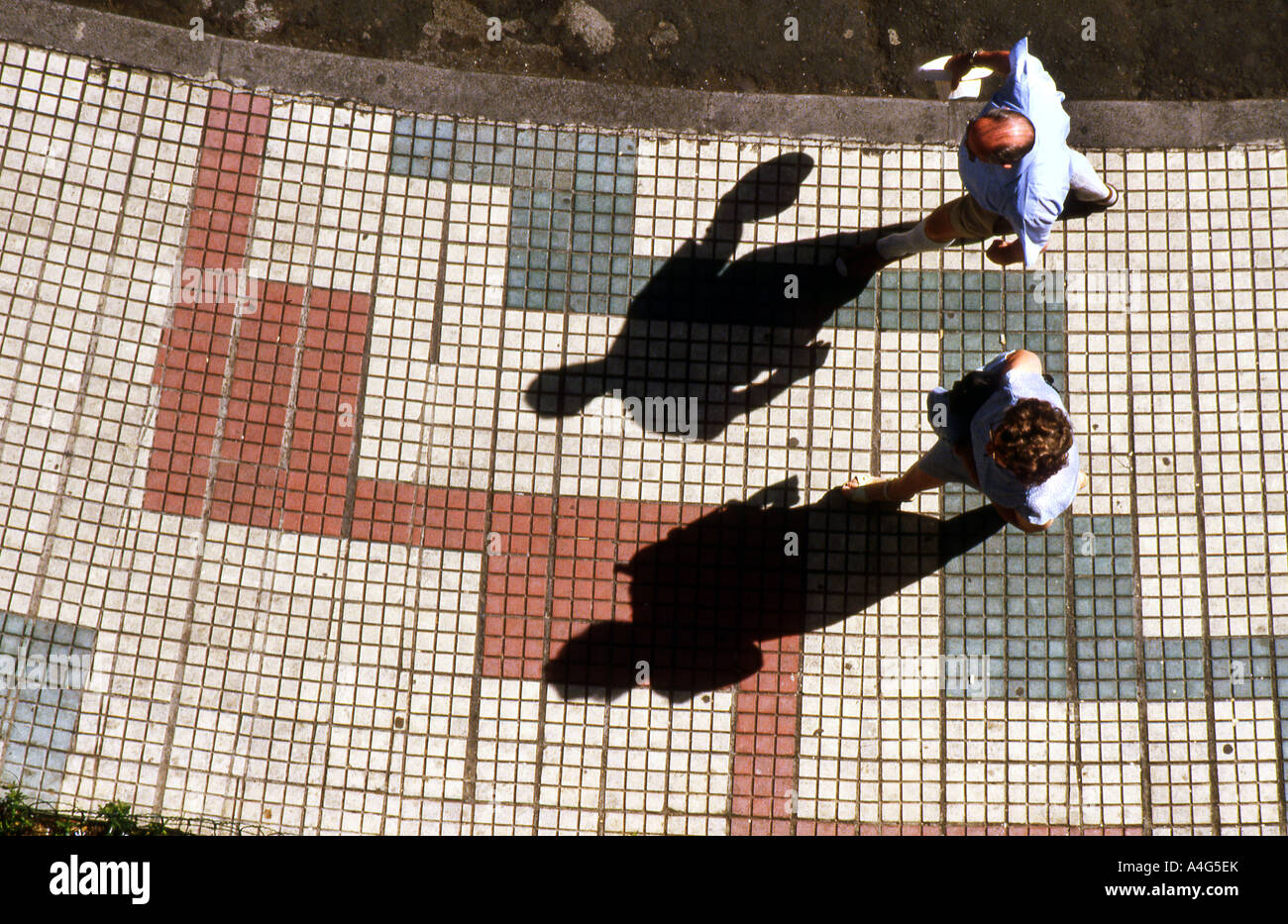 View from above of two people walking along sunlit sidewalk with long ...