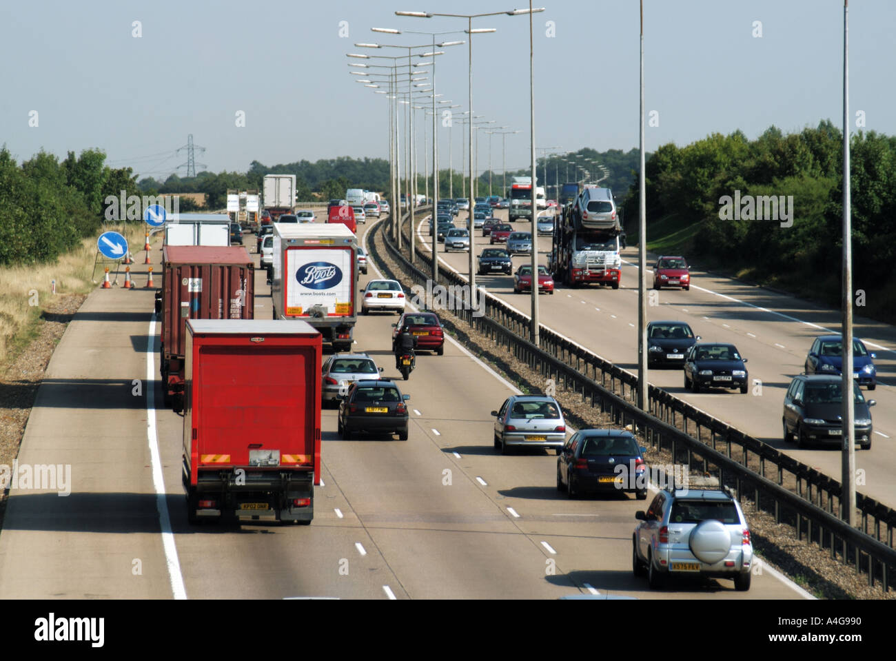 Back & front view from above on lorries trucks car traffic driving on busy three lane concrete motorway & road hard shoulder steel crash barrier UK Stock Photo